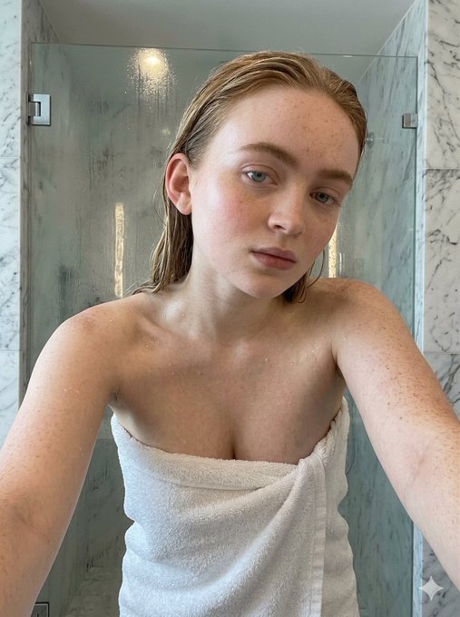 Close-up selfie of a person with wet hair wrapped in a white terry cloth towel in a bright bathroom, showcasing freckles and dewy skin.