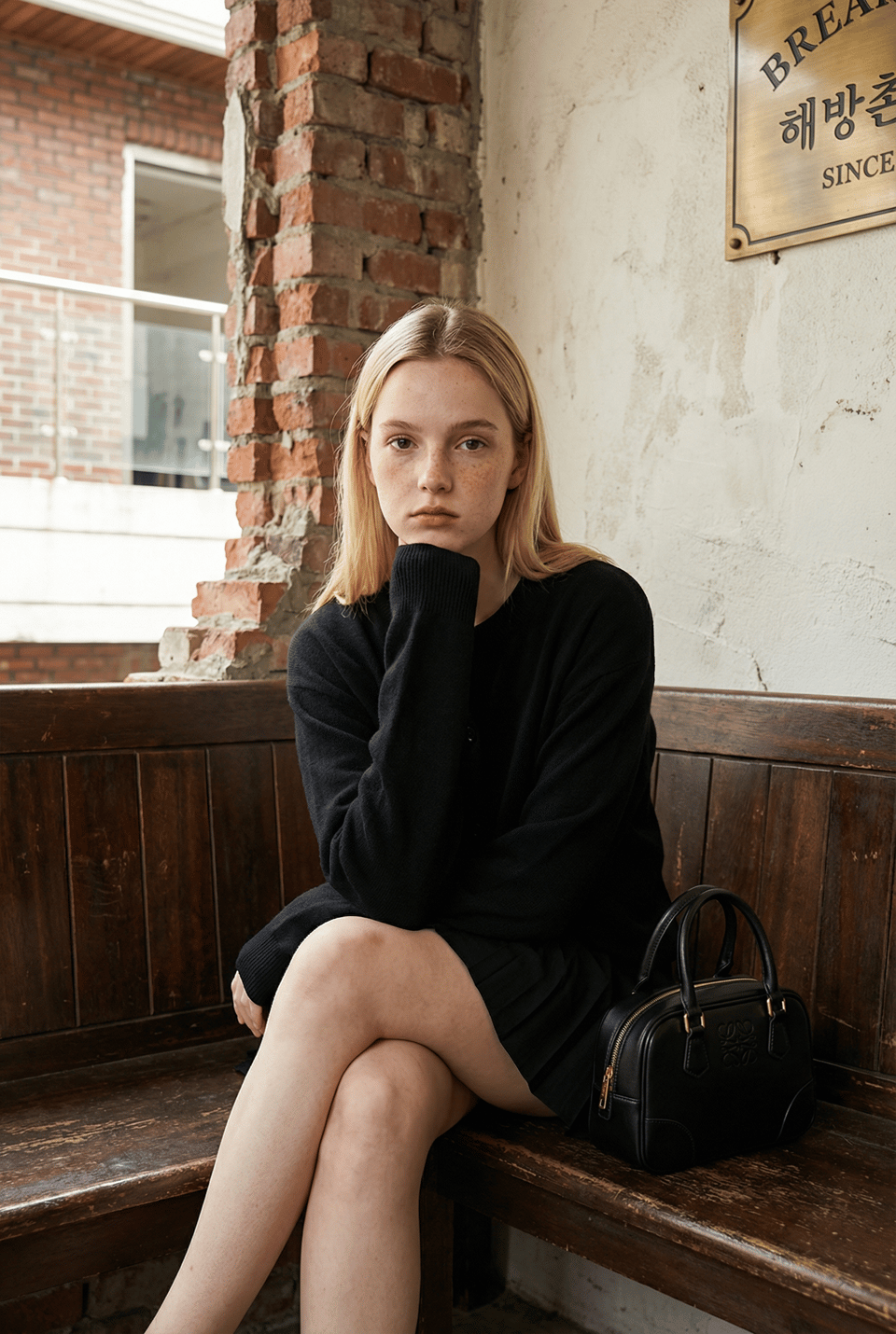 A young adult female sitting on a wooden bench in a vintage cafe, with light skin, freckles, and blonde hair, dressed in a black oversized sweater.