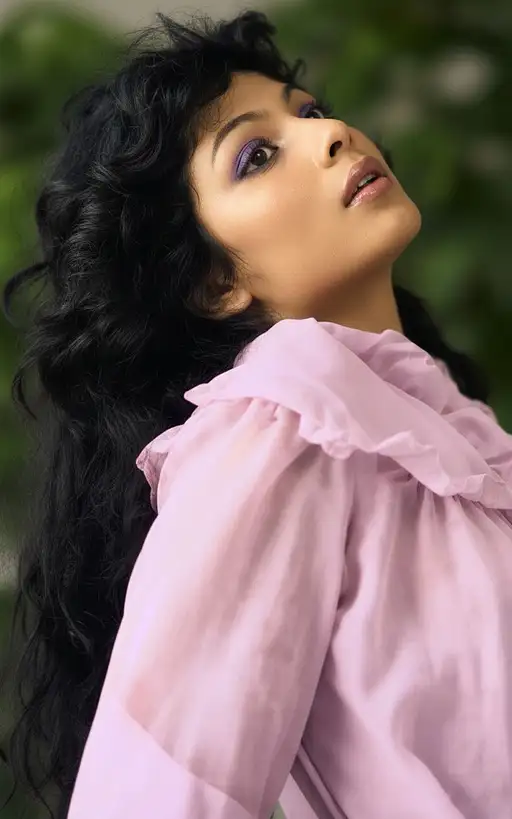 A captivating female model with glossy lips and piercing dark brown eyes, framed by abundant black hair and soft natural lighting.