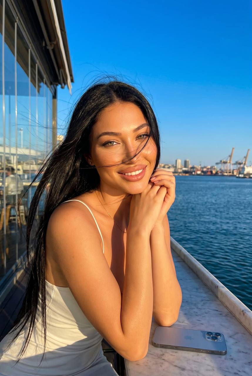 A woman in a white bikini leaning on a marble surface, with the harbor city skyline in the background, glowing in warm sunlight.