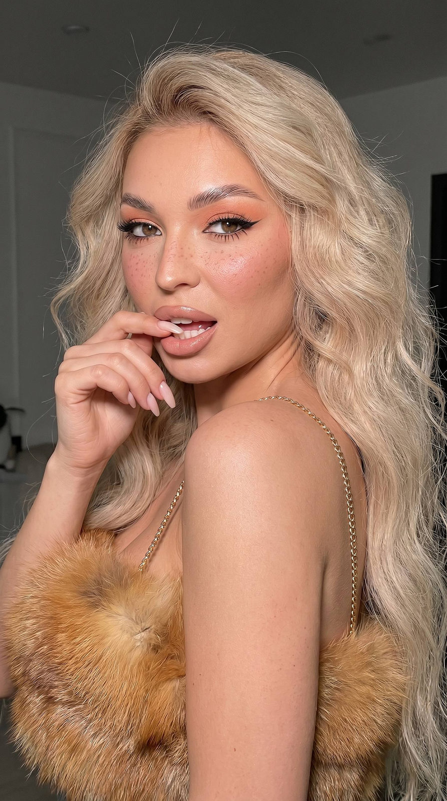 Close-up portrait of a girl with fox fur top and peachy eye makeup, playful gaze, and long waves of hair.