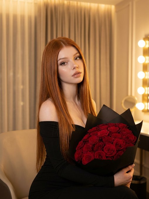 Portrait of a woman in an off-the-shoulder black dress holding deep red roses by a vanity mirror.