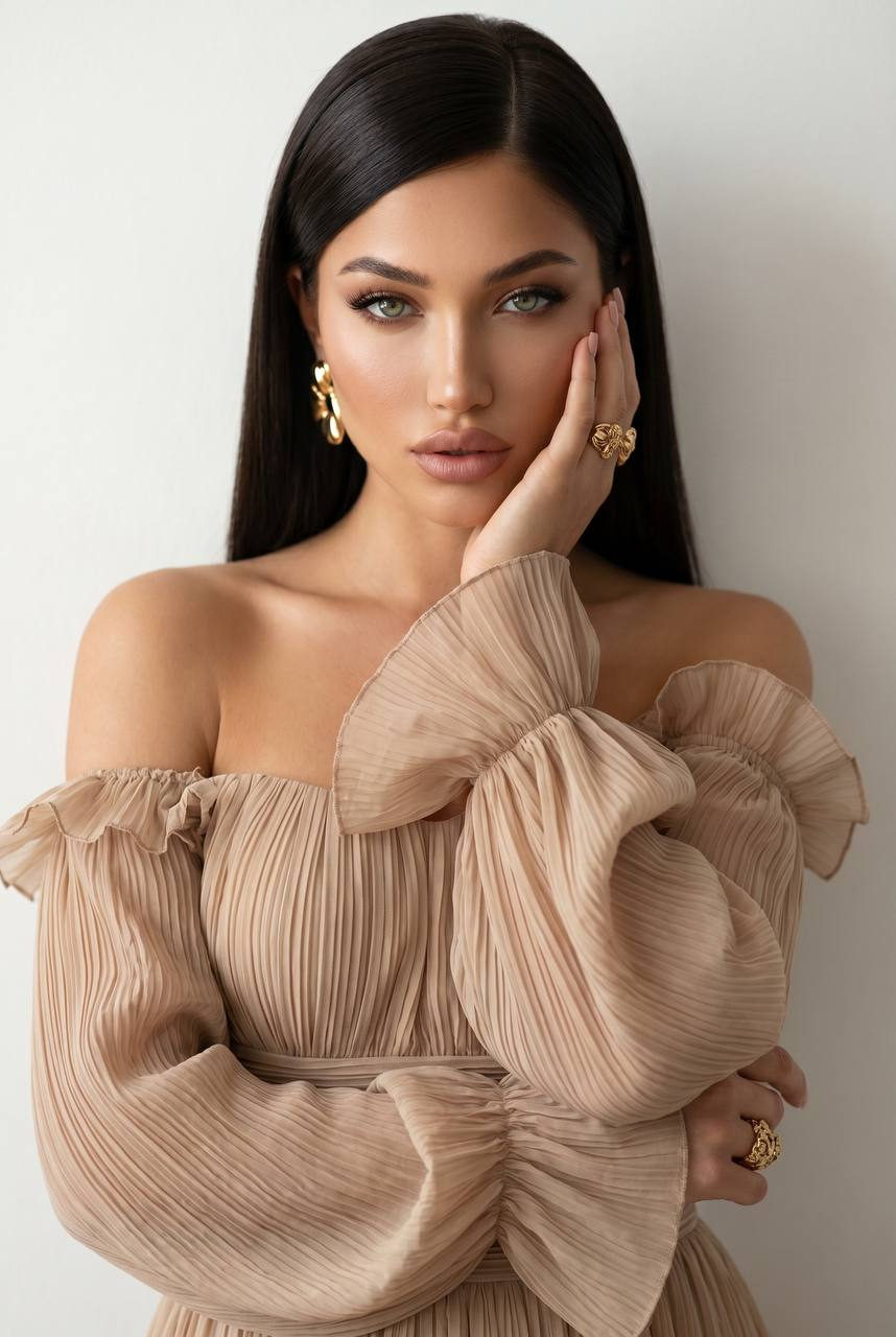 Close-up portrait of a woman in a beige pleated gown against a plain light wall, showcasing soft lighting and dramatic shadows.