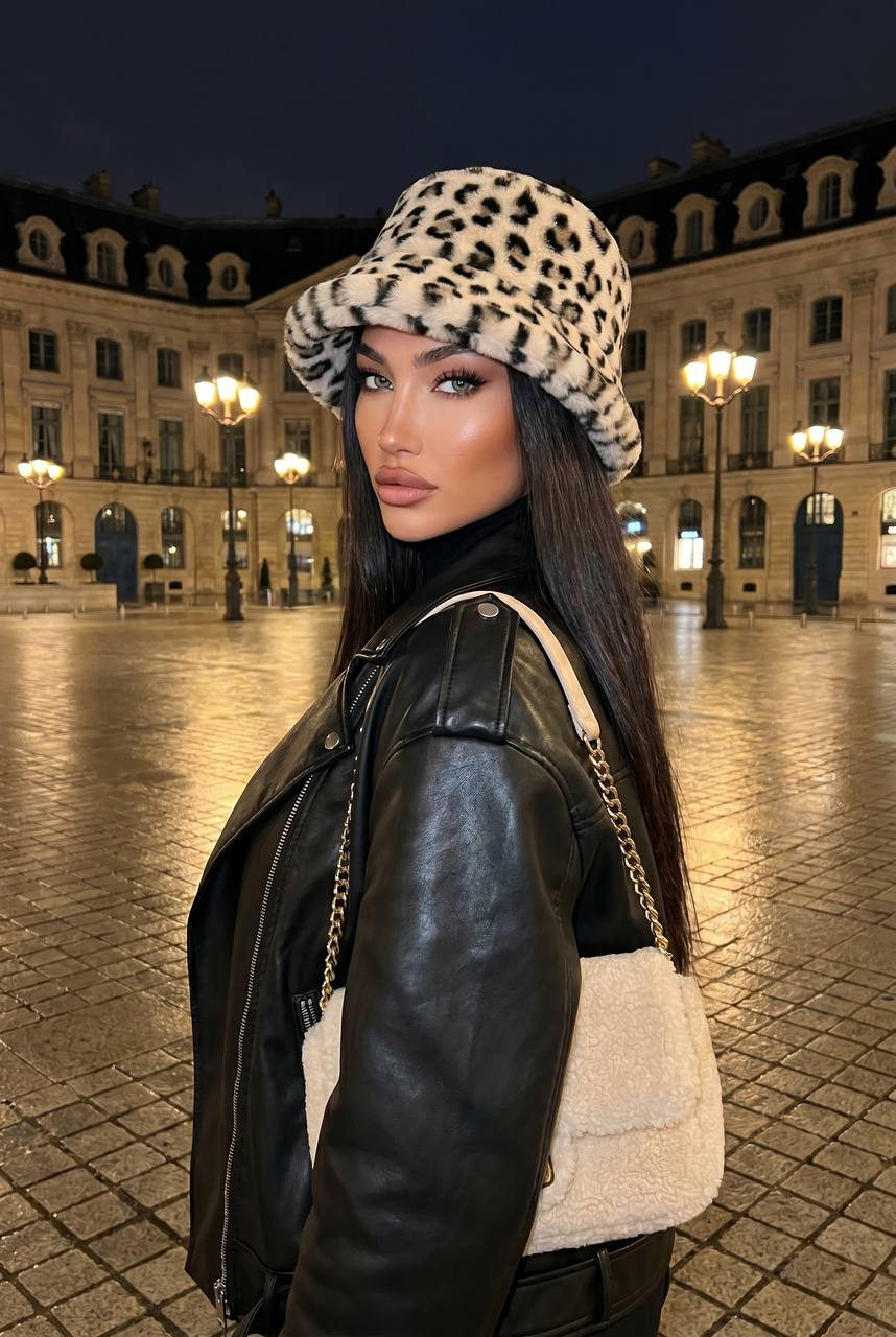Woman in a black leather oversized biker jacket looking over her shoulder in a European city square at night.
