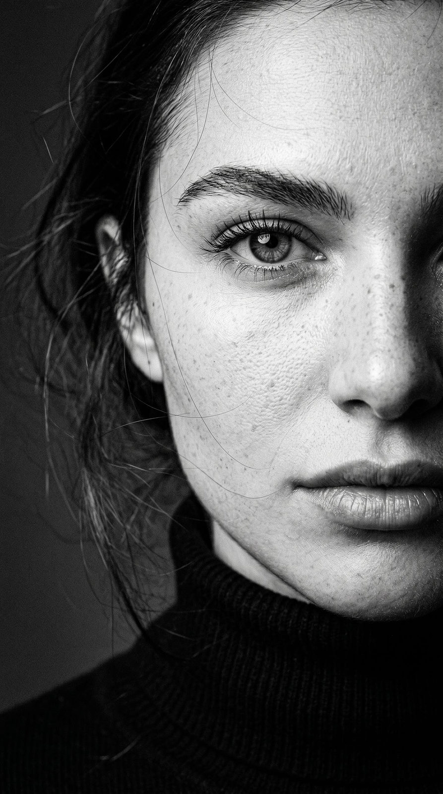 Close-up shot of a woman's face wearing a black turtleneck, captured in black and white with cinematic grain.