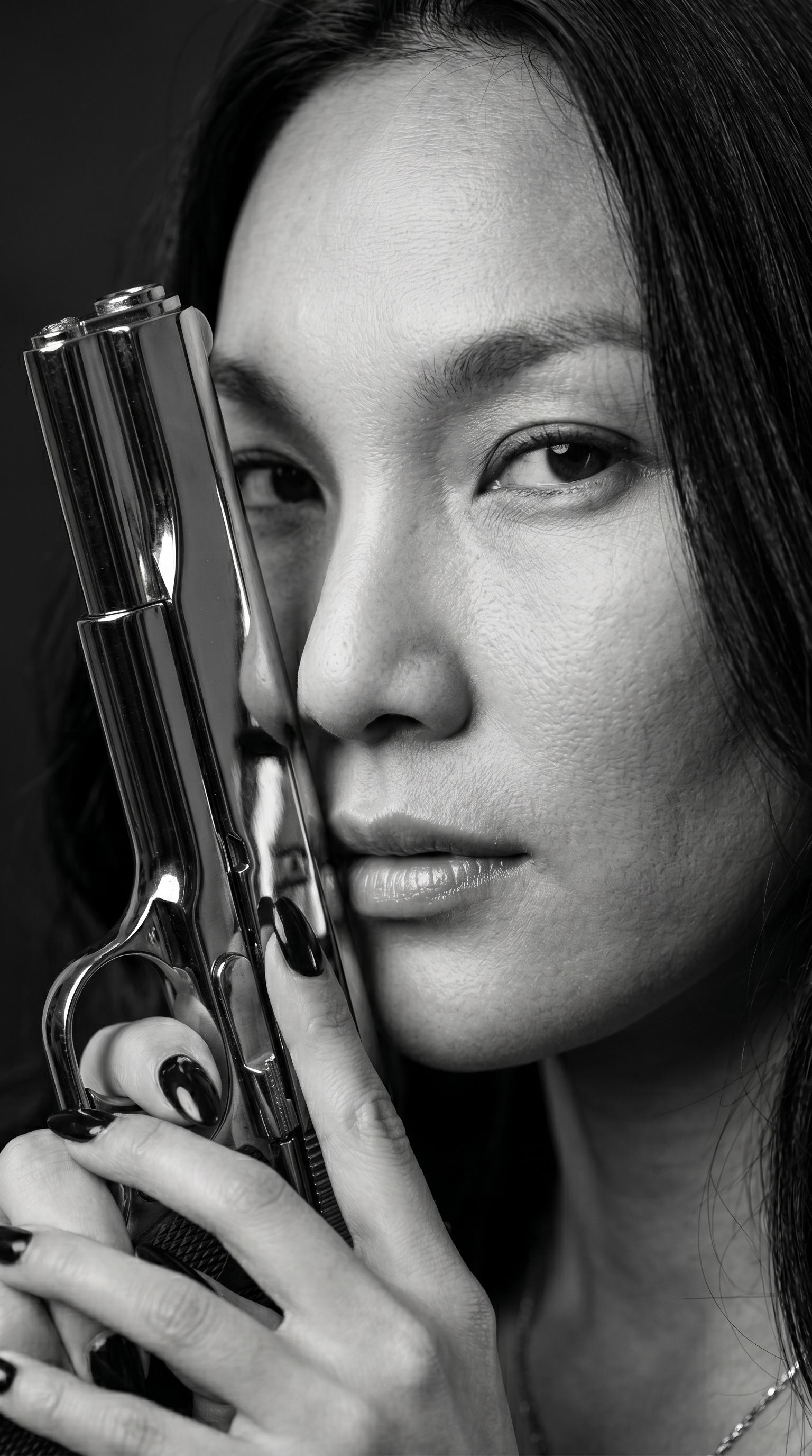 A black and white close-up of a person holding a polished metallic handgun near their face, obscuring features, with dramatic lighting.