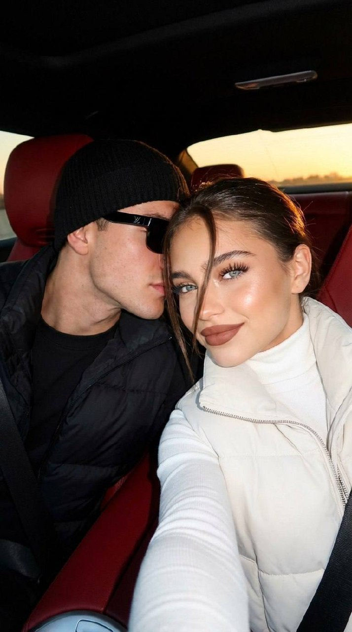 A stylish couple taking a selfie inside a luxury car at night, illuminated by golden hour light