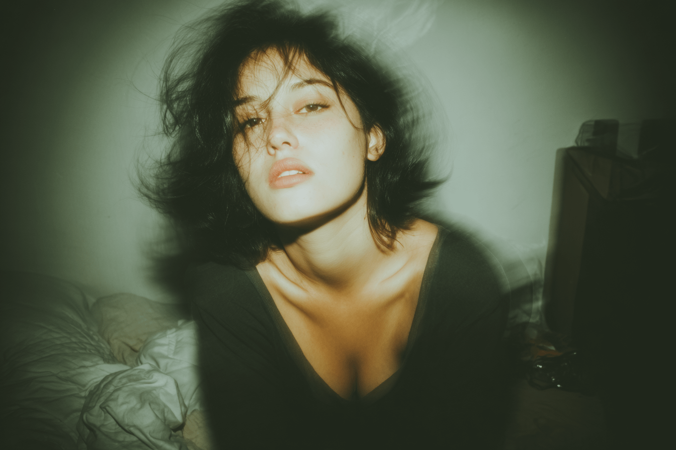 A modern, minimalist portrait of a woman in her bedroom, featuring a long exposure motion blur effect.