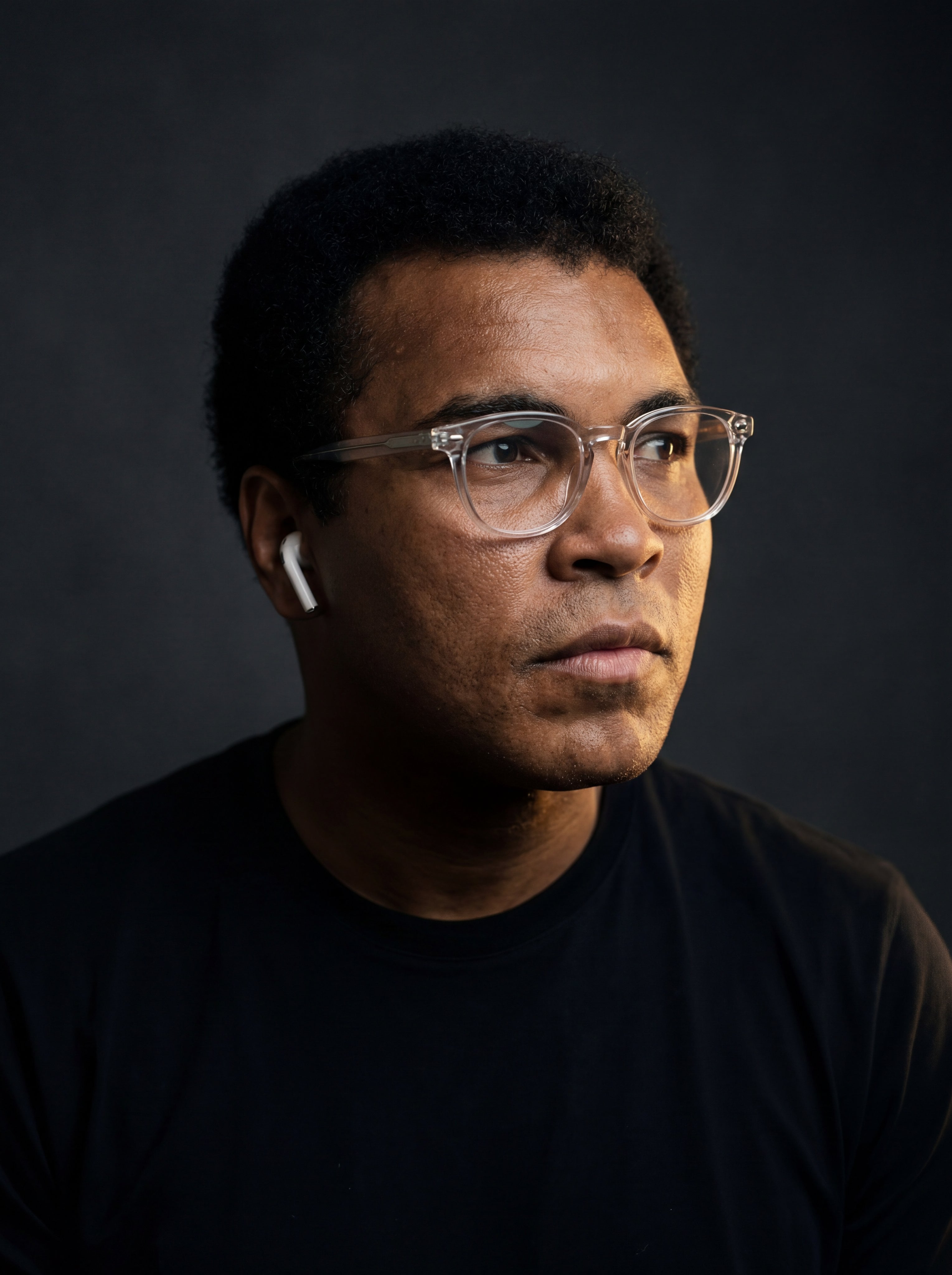A medium close-up portrait of a subject looking right with a soft matte black t-shirt against a dark gray background.