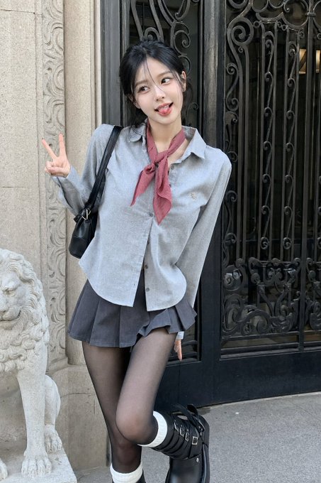A medium shot of a model in a grey outfit making a peace sign by an ornate gate and a stone lion statue.