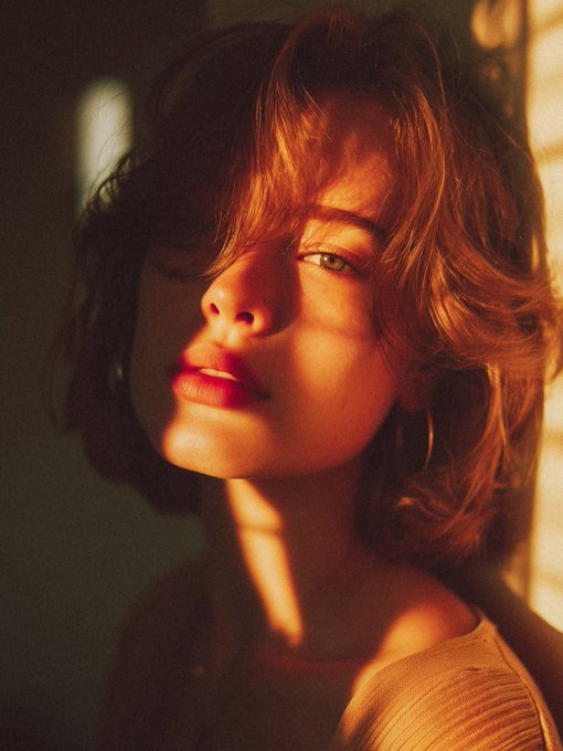 Close-up portrait of a woman with wavy hair partially obscuring her face, dramatic shadows and vibrant red lips.