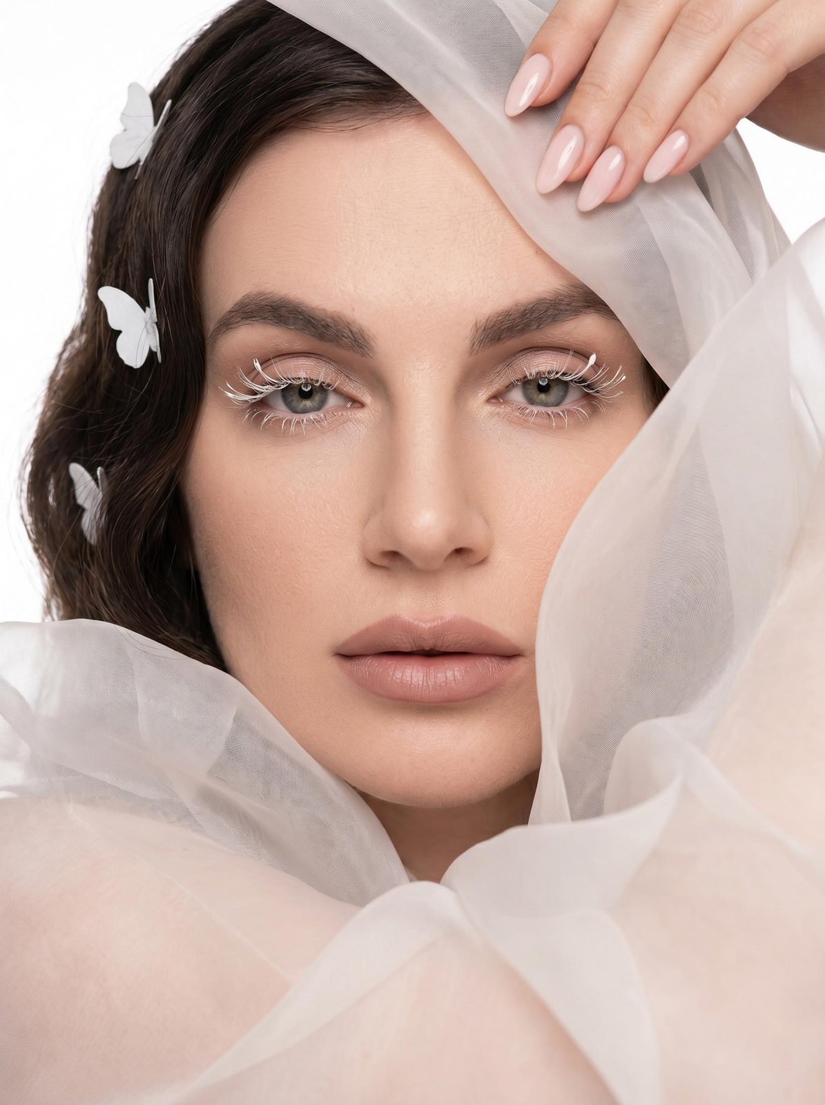 Close-up portrait of a woman with translucent white fabric framing her face, soft lighting on skin and makeup.
