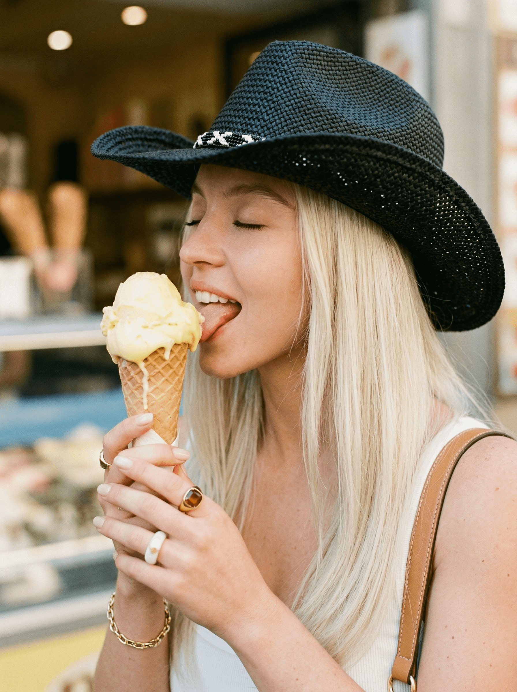 A woman in a casual outfit enjoying a colorful ice cream cone on a sunny street.